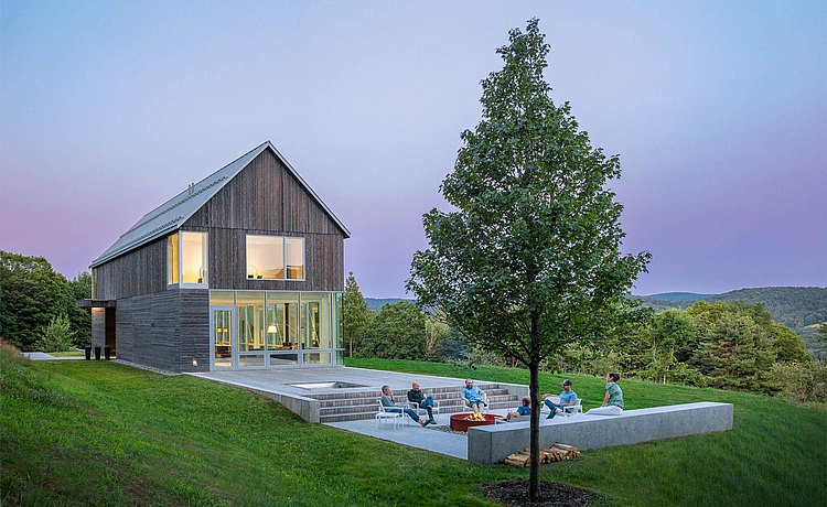 Exterior view of house in rural Vermont with people gathered around the fire pit.